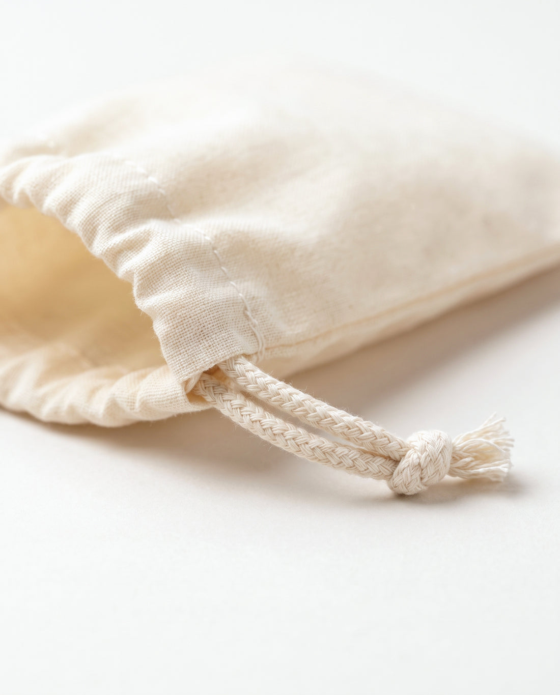 Close-up of the stitched drawstring channel and braided cotton cord knot on natural muslin