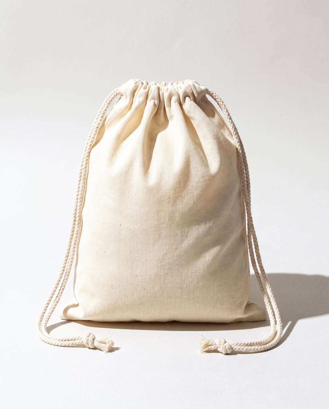 Plain natural cotton muslin double drawstring bag with braided cotton cords, white background
