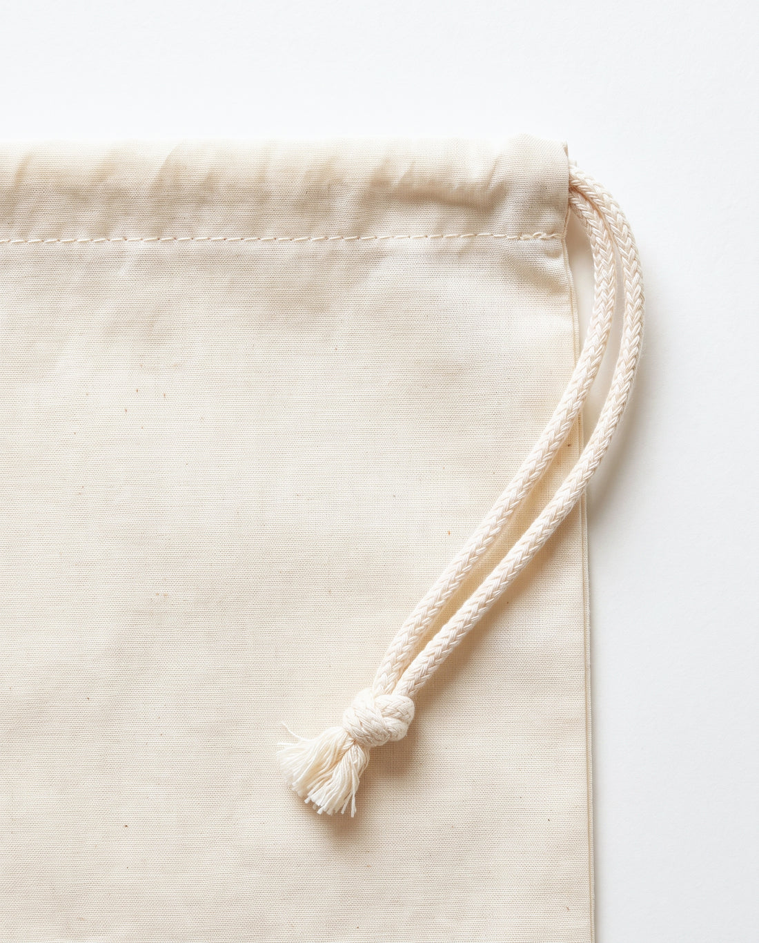 Close-up of the stitched drawstring channel and braided cotton cord knot on natural muslin